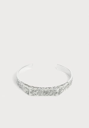 Bracelet manchette ouvert en argent avec des gravures florales et de vigne complexes le long de sa surface sur un fond blanc uni.