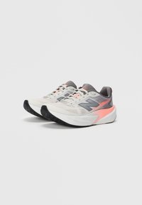 Une paire de chaussures de course blanches et grises avec des semelles noires et des accents corail, disposées côte à côte sur un fond uni.