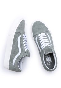 Grå mockasneakers med vita snören, signaturvit sidostrip, och gummisulor. Klassisk låg toppdesign med en texturerad yta.