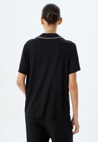 Zwart kortogige shirt met een kraag en witte piping langs de halslijn. Zachte stof, ontspannen pasvorm en eenvoudig design zonder patronen.