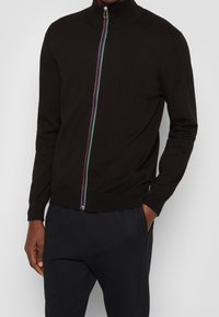 Svart zip-up tröja med hög krage, med en flerfärgad dragkedja och ribbade ärmslut. Tillverkad av mjukt, strukturerat tyg.