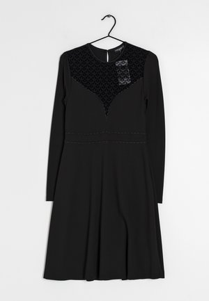 Robe noire à manches longues avec un tissu texturé sur le corsage, une taille cintrée et une jupe évasée. Tissu lisse avec des coutures apparentes.
