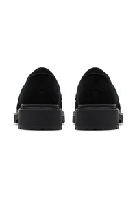 Ein Paar schwarze Wildlederslipper mit dicken, gerippten Gummisohlen von hinten auf einem weißen Hintergrund betrachtet.