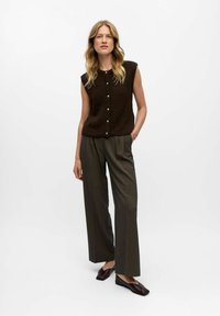 Braunes ärmelloses Stricktop mit Rundhalsausschnitt und Knöpfen an der Vorderseite, kombiniert mit hoch taillierten, weit geschnittenen gestreiften Hosen und dunklen Ballerinas.