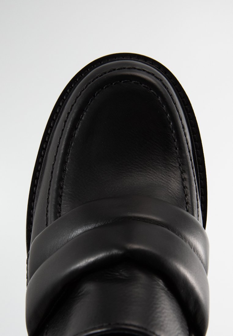 Czarna skórzana brog, z zaokrąglonym kwadratowym noskiem, ozdobnym przeszyciem i wyściełanym paskiem na górnej części.