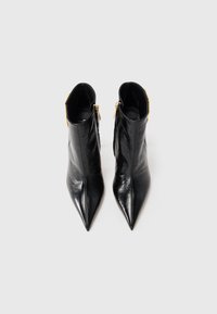 Black leather ankle boots with a pointed toe, side zipper closure, and gold hardware accents. Smooth texture with a sleek design.