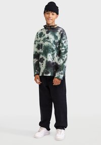 Long-sleeve tie-dye sweatshirt in green and black, paired with black jeans and white sneakers. Also features a black beanie.