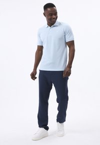 Hellblaues Polohemd mit kurzen Ärmeln, kombiniert mit dunkelblauen Hosen und weißen Sneakern. Das Hemd hat einen klassischen Kragen und ein dezentes Logo.