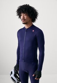 Marinefarbendes Fahrradtrikot mit langen Ärmeln, durchgehendem Reißverschluss, strukturierter Stoff und kleinem Logo auf der Brust, kombiniert mit schwarzen Handschuhen und Helm.