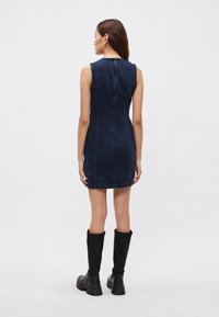 Tmavomodré rifľové šaty bez rukávov so zipsom na chrbte a tmavými švami. Nosené s čiernymi vysokými topánkami nad kolená s hrubou podrážkou.