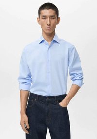 Light blue long-sleeve shirt with a collar, featuring button-down front and rolled sleeves, paired with dark blue denim jeans. Minimalist design.