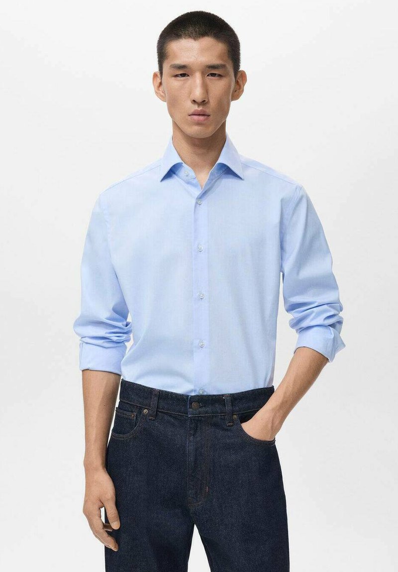 Light blue long-sleeve shirt with a collar, featuring button-down front and rolled sleeves, paired with dark blue denim jeans. Minimalist design.