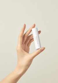 Baume à lèvres cylindrique blanc tenu dans une main, avec un design minimaliste et un texte noir indiquant le produit "NEEDLY". Surface lisse, finition mate.