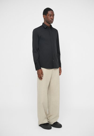 Μαύρο πουκάμισο με γιακά, συνδυασμένο με ανοιχτό μπεζ φαρδιά παντελόνια και μαύρα παπούτσια. Απλός σχεδιασμός, λείος υφαίν.