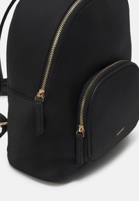 Black backpack made of smooth material, featuring a rounded shape, gold zipper accents, and a front pocket with a curved design.