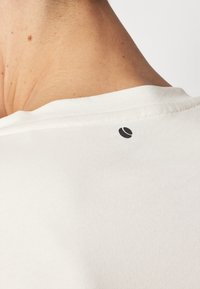 White t-shirt collar with visible stitching; logo featured on the back near the neckline in a contrasting black color. Soft texture.