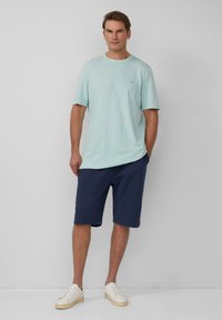 Jasno miętowa bawełniana koszulka z krótkim rękawem, zestawiona z granatowymi szortami i białymi trampkami. Prosty design bez wzorów.