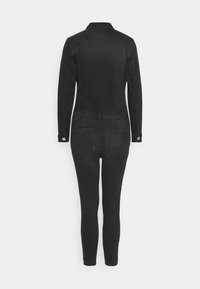 Combinaison en denim noir avec des manches longues, un col, des jambes ajustées et des poches au dos. Texture lisse avec de subtils détails de couture.