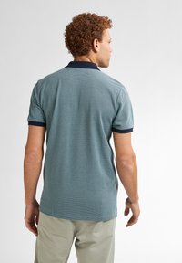 Polo tričko s krátkým rukávem v tyrkysovém vzorovaném materiálu, se námořnickým límcem a manžetami. Design má jemně texturovaný povrch a zakřivený lem.