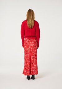 Ein roter gerippter Pullover kombiniert mit einem langen Blumrock, der ein rot-rosa Design aufweist und mit schwarzen Blumen akzentuiert ist. Getragen mit schwarzen Stiefeletten mit Absatz.