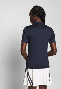Polo shirt blu navy con una texture liscia, maniche corte e colletto classico, abbinato a una gonna bianca svasata con strisce diagonali blu navy.