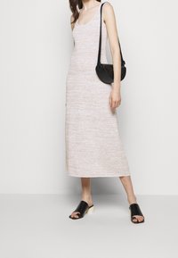 Abito lungo in maglia beige chiaro con scollatura a girocollo, abbinato a mule nere con punta aperta e tacco crema, e una borsa a spalla nera.