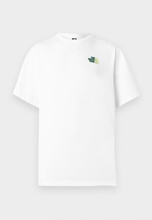 Göndör hajú, vitiligós személy fehér pólóban zöld "The North Face" logóval és világosbarna nadrágban, hátulnézetből.