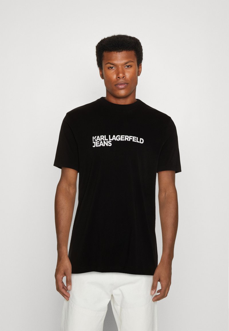 Fekete póló rövid ujjakkal, kerek nyakkivágással és fehér "KARL LAGERFELD JEANS" logóval az elején. Simaságú pamutszövet.
