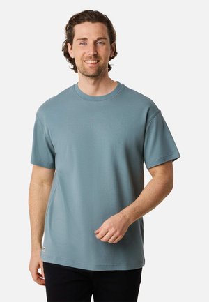 Helles blaugraues Baumwoll-T-Shirt mit Rundhalsausschnitt und kurzen Ärmeln, das eine lockere Passform aufweist und dezente Steppdetails an den Kanten hat.