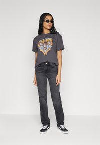 Γκρι γραφικό t-shirt με πολύχρωμο σχέδιο αετού, συνδυασμένο με σκούρα τζιν και μαύρα καμβά παπούτσια με λευκές σόλες.