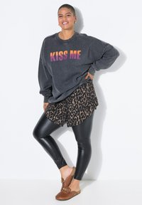Overmatig grote charcoal sweatshirt met 'KISS ME' print, gecombineerd met bruine luipaardprint shorts, zwarte leggings en bruine instap schoenen.