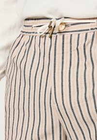 Pantaloni a righe con strisce verticali nei colori rosa pastello e blu navy, dotati di una vita regolabile con cordoncino, due tasche laterali e un tessuto testurizzato.