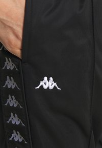 Svarta träningsshorts med en texturerad yta, utrustade med en vit broderad logotyp och ett mönstrat sidofält i grått.