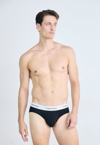 Fekete pamut bugyi fehér Calvin Klein derékpánttal. A fazon szoros, sima textúrával és minimális dizájn elemekkel rendelkezik.