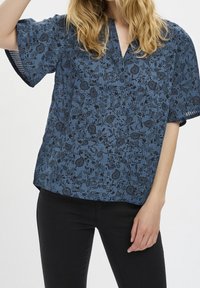 Top stampato floreale blu in tessuto leggero, con maniche corte, scollatura a V e vestibilità ampia. Contrasto di colore tra nero e blu.