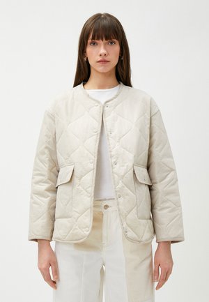 Giacca trapuntata beige con scollo rotondo, bottoni a pressione e due tasche frontali. Realizzata in tessuto morbido e strutturato, caratterizzata da un motivo a diamante.