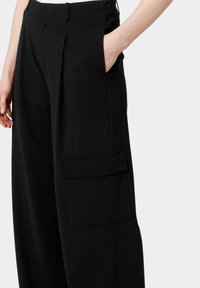 Černé cargo kalhoty s volným střihem, předními sklady a boční kapsou se zapínáním na klopu. Vyrobené z hladkého tkaniny s minimální texturou.