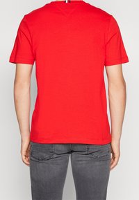 T-shirt rouge à manches courtes en coton, avec un col rond et un discret détail de couture à l'arrière. Associé à un jean gris.