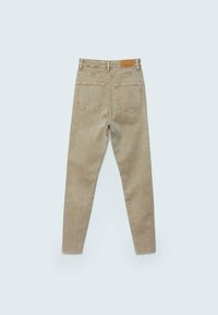 Jeans ajustados beige con un acabado desvanecido, cinco bolsillos y dobladillo sin rematar. Presenta una etiqueta de cuero en la cintura.