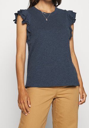 Navy blue short-sleeve top with ruffle accents on shoulders, made from a soft fabric. Crew neck design, relaxed fit, paired with tan pants.