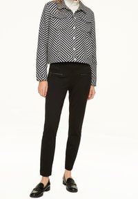 Sort og hvid stribet cropped jakke med to brystlommer, parret med sorte slim-fit bukser med lynlås-lommer og sorte loafers.