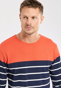 T-shirt à manches longues avec un haut rouge et des rayures horizontales bleu marine et blanches sur le corps, fabriqué en coton doux.