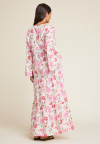 Maxikjole i hvit bomull med rosa og røde blomstertrykk. Lange ermer med volanger og en lagdelt skjørt. Enkel rund halslinning.
