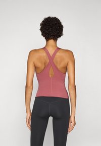 Tajta vinröda linne med korsade axelband och en nyckelhålsdetalj på ryggen, kombinerat med svarta leggings. Slät tyg med matt finish.