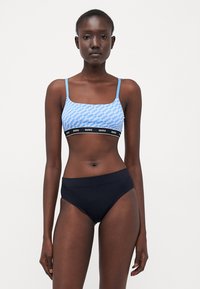 Blue sports bralette featuring a repeating "HUGO" logo pattern and thin straps, paired with high-waisted black briefs with a smooth finish.