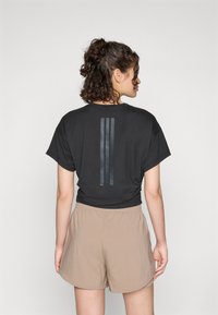 La t-shirt nera a maniche corte presenta un design a righe nere opache sul retro, abbinata a pantaloni corti leggeri beige.
