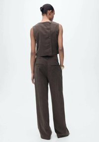 Bruine cropped top met knopen op de rug, gecombineerd met bijpassende wijde broek. De stof lijkt textuur te hebben, waardoor er een samenhangend outfitontwerp ontstaat.
