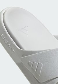 Valkoinen liukuva sandaali, jossa on teksturoitu pinta, muotoiltu muotoilu ja Cloudfoam-tyynytys. Varustettu korotetulla logolla ja minimalistisilla yksityiskohdilla.