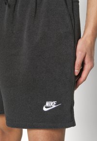 Pantalones cortos de tela de rizo negra con una cinturilla elástica, que presentan un logo blanco de Nike bordado en la pierna derecha. Longitud corta y textura suave.