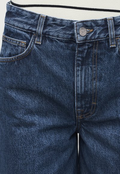 Predný pohľad na tmavomodré rifle z denimu so viditeľným gombíkom, zipsovým zapínaním, slučkami na opasok a prešívaním vrecka vpredu.